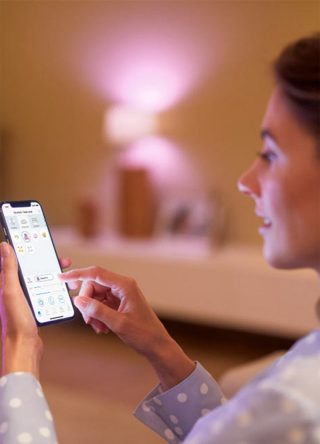"Woman controlling smart LED lighting via smartphone app, adjusting pink ambient glow for personalised home atmosphere."
