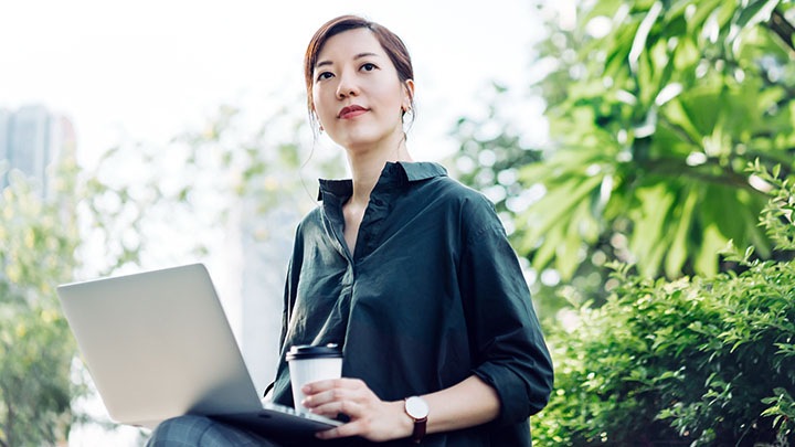 Asiatische Geschäftsfrau sitzt auf der Bank und arbeitet am Laptop