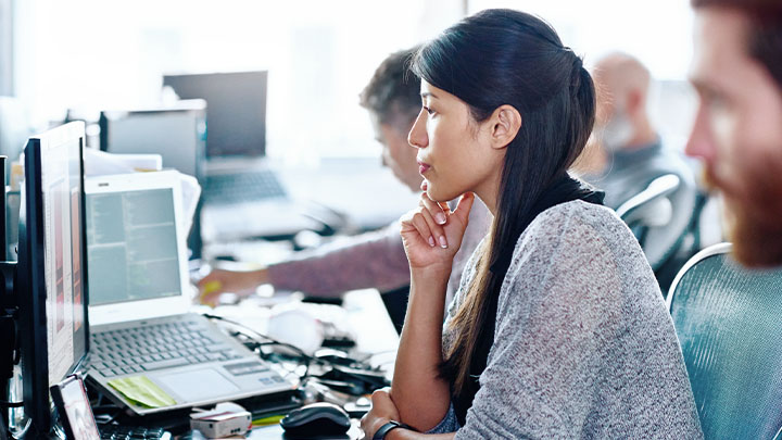 Eine Mitarbeiterin konzentriert sich in einem belebten Büro auf ihren Computerbildschirm
