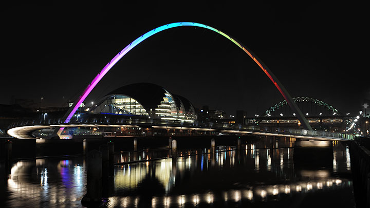 Gateshead Millennium bridge illuminated with rainbow lighting at nightime