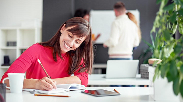 A happy woman working in an office with co-workers busy behind her