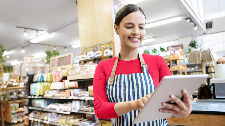 Ein Supermarktangestellter in einer Schürze steuert die Beleuchtung des Geschäfts auf einem Tablet