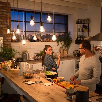Ein Paar im Gespr&auml;ch unter einer Deckenlampe mit Philips Vintage LED-Lampen, die ein gem&uuml;tlich warmes Schimmern erzeugen.