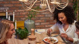 Cozinha moderna com luzes pendentes LED de estilo vintage que iluminam duas mulheres a jantar, criando um ambiente acolhedor e convidativo.