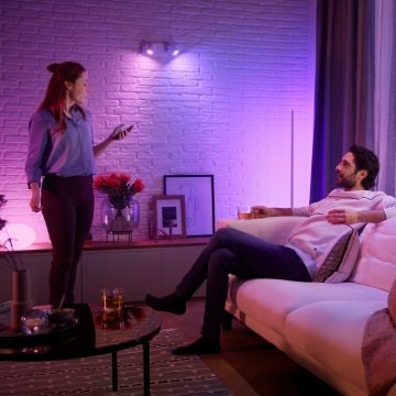 Ein Paar entspannt sich in einem mit smarten Lampen von Philips Hue lila und rosa beleuchteten Wohnzimmer. 