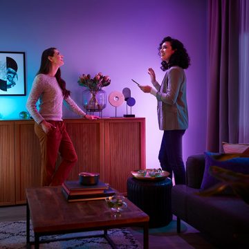 Kobieta tworzy w salonie kolorową scenę świetlną składającą się z różowego i fioletowego światła, korzystając z aplikacji Philips Hue na swoim smartfonie. 