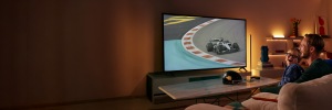 Un padre y su hijo sonrientes ven en la televisión una carrera de automovilismo con la iluminación inteligente WiZ detrás de la pantalla y en los estantes cercanos.