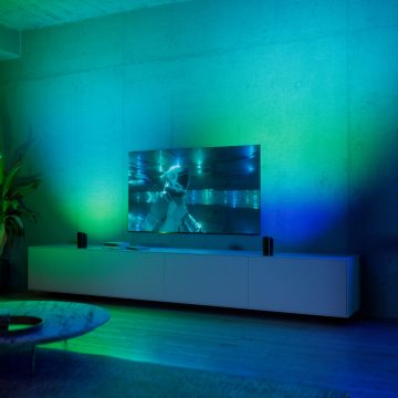 Zwei Hue Play Wallwasher auf jeder Seite des Fernsehers erzeugen ein lebhaftes, grünes und blaues smartes Licht. 