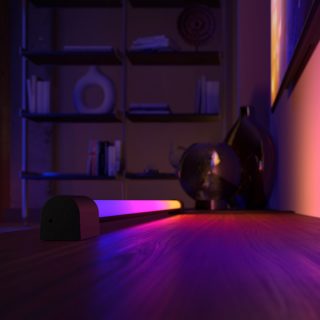 Hue Play Gradient Light Tube unter einem Fernseher erzeugt ein Licht in den Farben pink, violett und gelb. 
