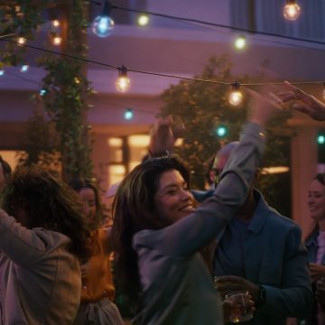 Eine Frau tanzt auf der Terrasse unter dem blauen, pinken und weißen smartem Licht der Festavia Globe Outdoor Lichterkette.