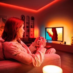 Une femme joue aux jeux vidéo avec un éclairage immersif sur le mur derrière le téléviseur.