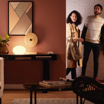Een stel komt een woonkamer binnen, die is verlicht met het slimme warmwitte licht van een Philips Hue lamp.