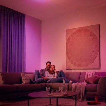 Een stel dat op een bank ontspant, omgeven met slimme zachtroze en paarse verlichting.