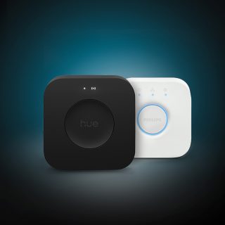 Nieuwe Hue Bridge Pro en Philips Hue Bridge voor bedieningssystemen voor slimme woningverlichting. Een persoon die slimme Philips Hue verlichting bedient met behulp van de Hue app op een smartphone. Een witte Philips Hue smart button op een tafel naast een laptop.