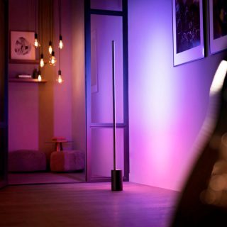 Eine Philips Hue Signe Gradient Stehleuchte taucht eine Wand in ein sanftes, pinkes und violettes smartes Licht.