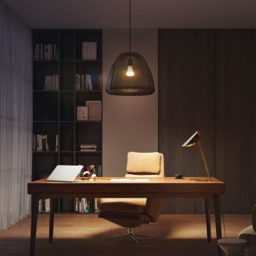 Un bureau à domicile avec table et chaise éclairés par une lampe à poser et une suspension connectées diffusant une lumière douce et chaleureuse.
