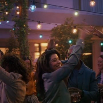 A woman dances on a patio under strings of Festavia outdoor globe party lights glowing in blue, pink and white smart light.