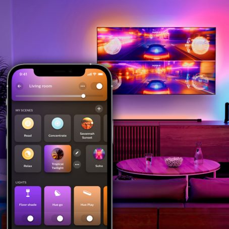 Een kleurrijk verlichte ruimte met een aan de wand gemonteerde tv. Het scherm is gedeeld voor een racegame. Een overlay van de Hue app met het tabblad Home.