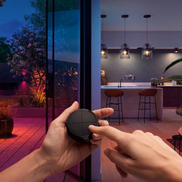 Handen die een Tap-draaischakelaar vasthouden om tegelijkertijd de slimme verlichting in een keuken en achtertuin te bedienen