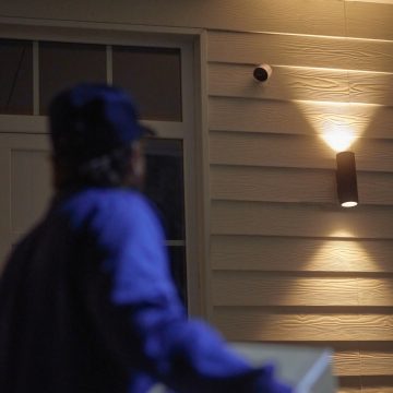 Curier care se îndreaptă către o ușă de la intrare protejată de o cameră Philips Hue Secure