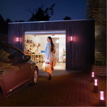 Kvinna som går med en påse matvaror från en bil mot ett starkt upplyst garage