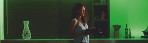 Person holding bowls in a kitchen with green LED strip lights illuminating the countertop and shelves with utensils and bottles.