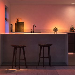 Smart kitchen lighting illuminates countertop and backsplash, highlighting sink area, fruit bowl, and kitchen accessories with colored light.