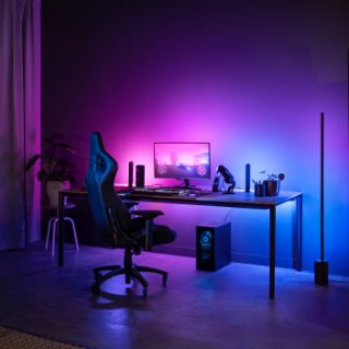Gaming desk setup in a living room illuminated by smart lighting, creating a vibrant ambient glow with purple and blue tones.