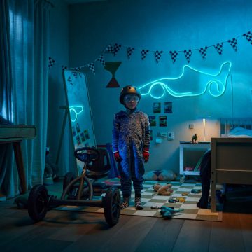 Un jeune garçon se tient à côté d’un kart dans sa chambre sur le thème de la course, éclairée par une bande flexible connectée WiZ bleue en forme de voiture de course.