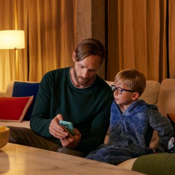 En pappa visar sin telefon för sin lille son i soffan. En lampa med en WiZ Smart Bulb ger ett varmt ljus.