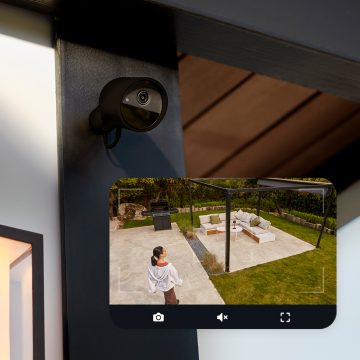 Et Hue Secure kamera monteret på en væg og et livebillede fra kameraet, der viser en kvinde i en baghave.