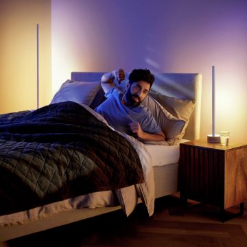 Mann wacht im Bett auf, während zwei smarte LED-Lampen einen Sonnenaufgang imitieren