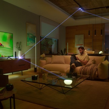 Mann auf dem Sofa im Wohnzimmer mit seinem Smartphone in der Hand. Die Verbindung der Hue Bridge zu den Lichtpunkten ist visualisiert.