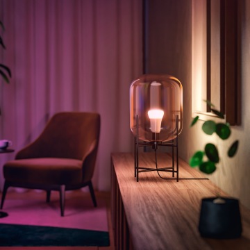 Philips Hue White & Color Ambiance Lampe in einer Tischleuchte auf einem Sideboard im Wohnzimmer.