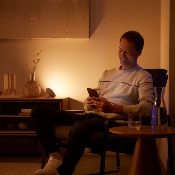 Ein Mann entspannt sich auf einem Stuhl, eingehüllt in warmweißes smartes Licht von Philips Hue.