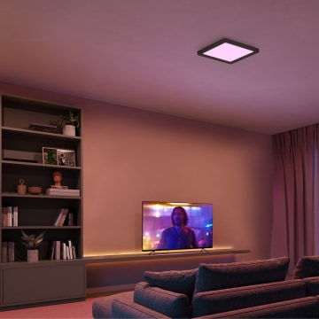 Schwarze, quadratische Deckenleuchte im Wohnzimmer mit Fernseher, eingestellt auf violettes Licht