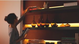 Woman reaching for a book on a shelf with undercabinet lighting.