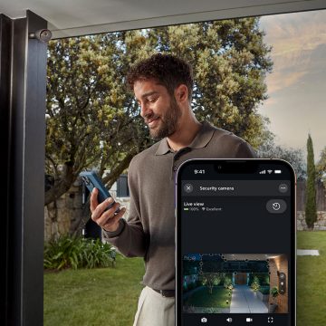 A man monitors a live view of a backyard on his smartphone using the Hue app.
