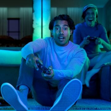 A gamer plays a game on a triple-monitor setup using Hue gradient lighstrips and light bars.