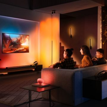 Three people sitting on a sofa watching TV with surround lighting.