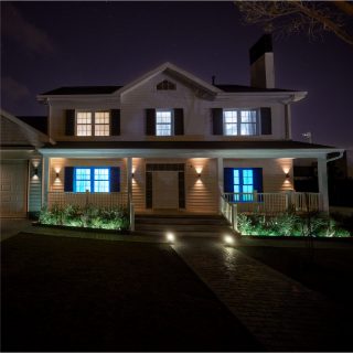 An intruder approaches a front door lit with two wall lights shining bright warm smart light.