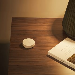 A white Philips Hue smart button placed on a table next to a laptop computer.
