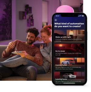 Two people sitting on a sofa in a living room with smart lighting, viewing automation options on a mobile app screen.