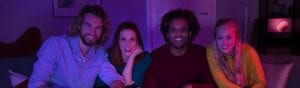 A group of people watching TV in a living room with purple and pink smart lighting illuminating the space.