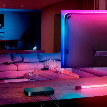 The Hue sync box 8K sits on a console table next to a TV screen in a living room.
