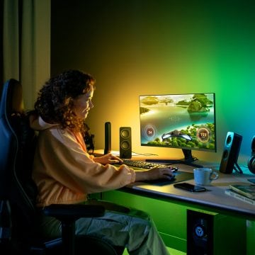 Woman sitting at gaming desk with green and yellow Philips Hue smart lighting
