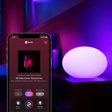A smart lamp on a side table with a mobile device displaying the Sync tab in the Hue app