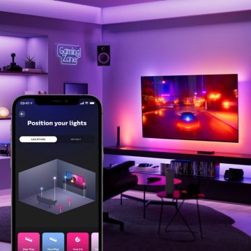 Overlay of the Hue app's Entertainment area creation screen on a living room with wall-mounted TV displaying a racing video game.