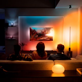 A couple watching TV with immersive TV surround lighting glowing in red, orange, and yellow smart light.