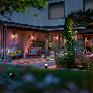 Outdoor smart wall lights mounted on patio walls and pathway lights illuminate the backyard seating area and garden plants.